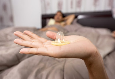 man lying on bed looks at a hand holding protection