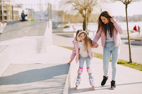 woman holding girl child's hand while she is rollerblading