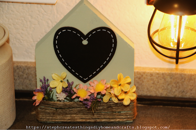light green painted wooden house with heart embellishment, twine, and artificial flowers