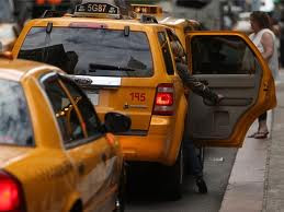 rear view of two yellow taxicabs, parked along the curb, one behind the other, with a passenger either getting in or out of the lead cab.