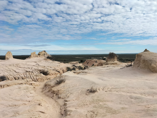 View of sand geological formations with flat vegetation of Lake Mungo visible in the distance