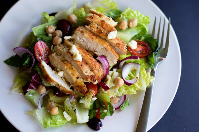 The completed Ultimate Greek Salad with Chicken on a white plate with a for to the side.