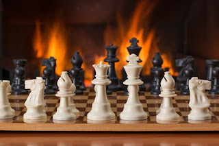 Chess pieces on a board with a fire in the background photo by stevepb at https://pixabay.com/photos/chess-board-game-fireside-strategy-2489553/