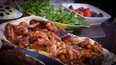 roasted chicken wings on a white color tissue paper in a tray besides coriander tray