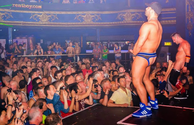 guy jacking off on stage for an audience wearing blue sneakers and jockstrap