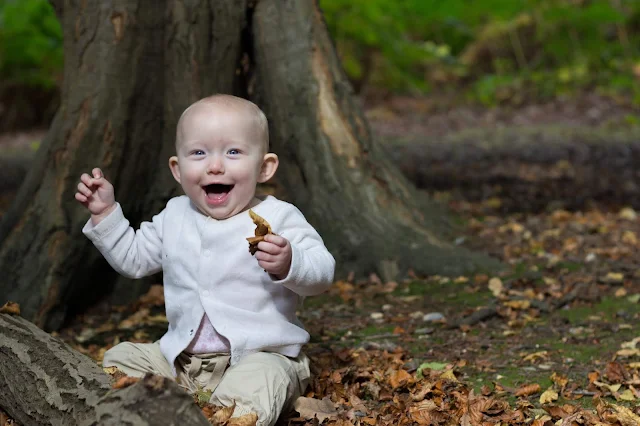 A laughing baby sitting in leaves in a forest perfect for Instagram