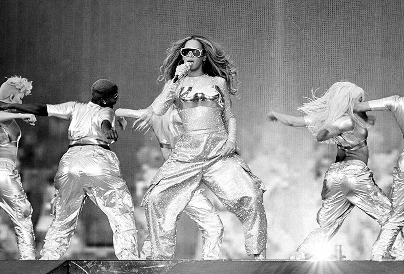 A shot of Beyoncé performing on the Renaissance World Tour. Beyoncé is performing “Formation” wearing a silver Loewe outfit with a metallic breast plate.