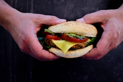 A Smoky Red Pepper and Cheese Bean Burger in a bun with pesto, slices of tomato and a slice of melted cheese