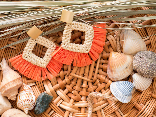 A pair of beach-inspired earrings with yellow tassels surrounded by shells.