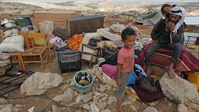 Un hombre palestino y sus dos hijos están sentados sobre los escombros de su casa destruida por el régimen de Israel.