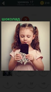 В руках у маленькой девочки большая плитка шоколада, которую она ест