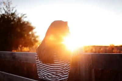 An image of a girl with black and white top looking the sunset from the terrace- sad girl dp