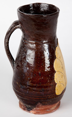 A tall brown ceramic jug with handle and off white leaf pattern on the front.