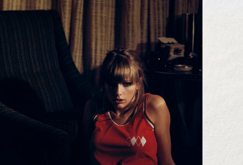 Taylor Swift sat in the dark, wearing a red tank top with a diamond motif.