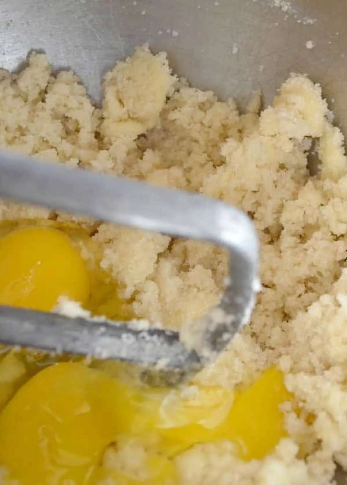 Creamed Butter and Sugar in a stainless steel mixing bowl with 2 whole eggs broken on top.