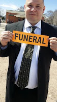 bald guy in black suit holding orange funeral sign classy undertaker mortuary home mortician tinder