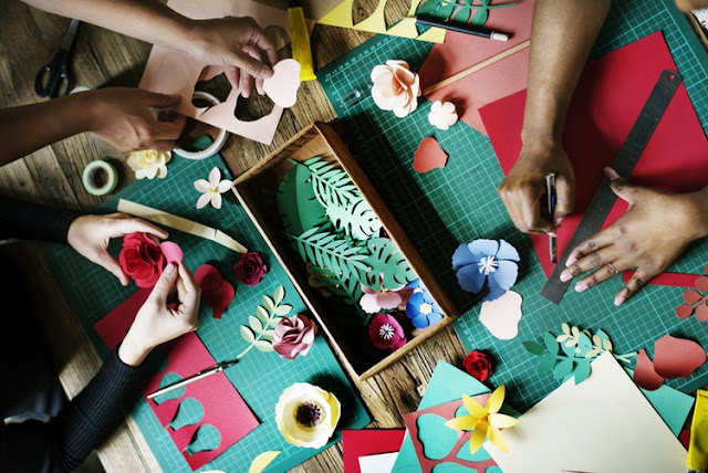 Paper crafts being done around a table with lots of different hands making things