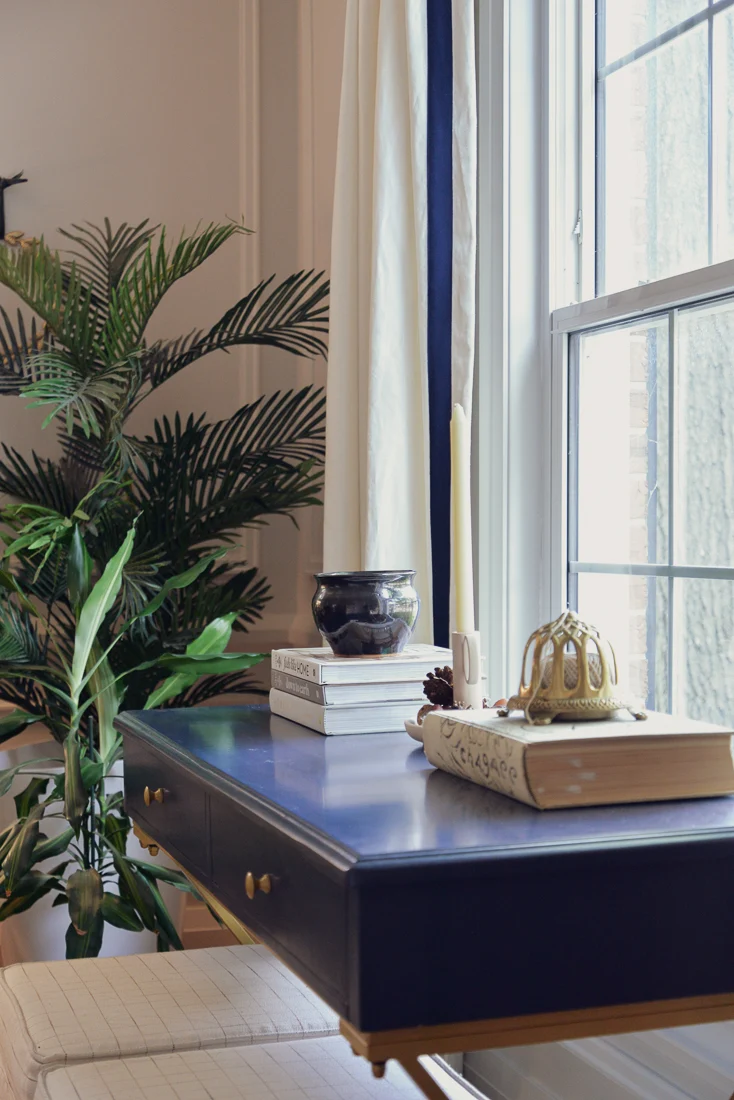 blue desk in front window stacked with books and pottery, candlestick, and vintage twine holder