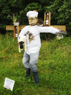 A scarecrow dressed as a chef with a sheep under one arm