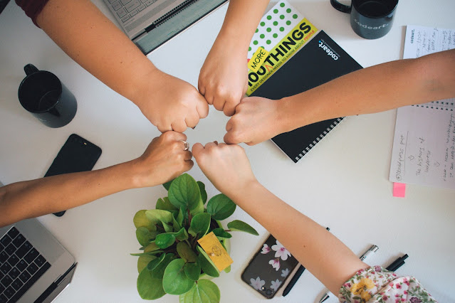 Five individuals join their fists in a gesture that promotes teamwork.