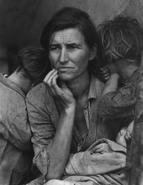 Foto em preto e branco, retrata uma mulher com uma mão no rosto, carregando um de seus filhos, e com os outros dois, cada um de um lado, apoiando as cabeças nos seus ombros com os rostos escondidos
