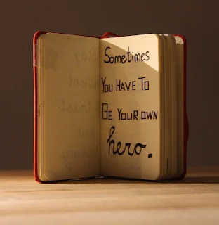 A notebook with the words "sometimes we have to be or own hero" written on the page.