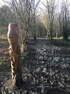 Muddy path with wood carving of an owl in the middle of it.