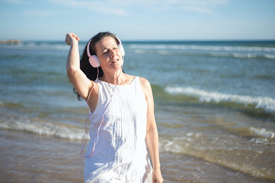 woman in white dess walking on the beach with headphones