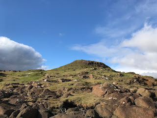 A photo of a hill with some rocks in the foreground - a view of Tickleness Point from the rocky seashore.  Photograph by Kevin Nosferatu for the Skulferatu Project.