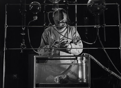 Lionel Atwill in The Vampire Bat (1933). He's wearing a lab coat and standing behind glass scientific equipment.