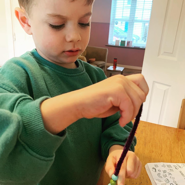 Little boy threading wooden beads onto a purple pipe cleaner