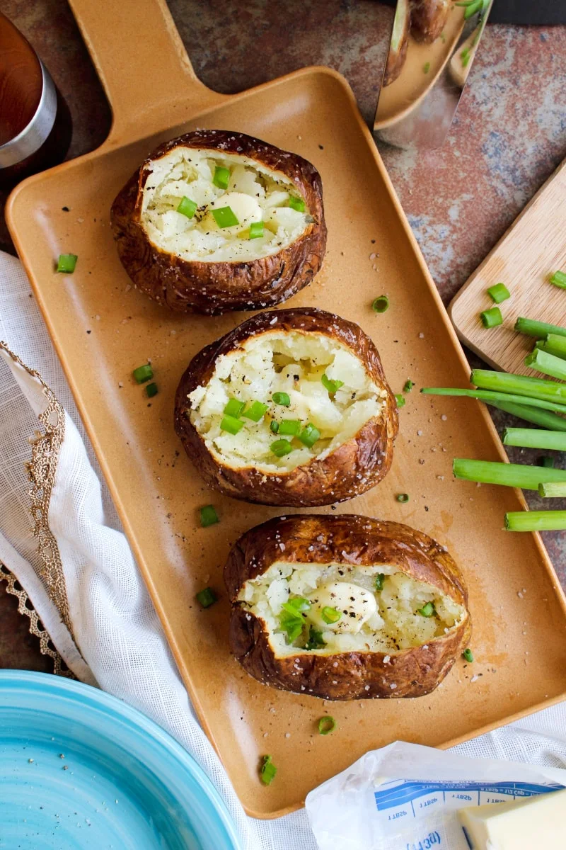 These baked potatoes cooked in the air fryer have a perfectly cooked fluffy inside and an irresistible crispy salty skin. You can eat them as a side dish or enjoy them as a light main dish! #airfryer #bakedpotato #sidedish