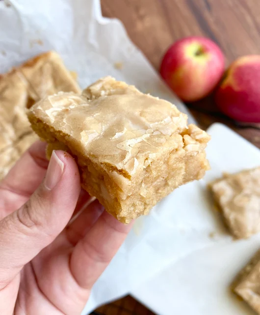 Hand holding a maple glazed apple blondie with a bite taken out of it.