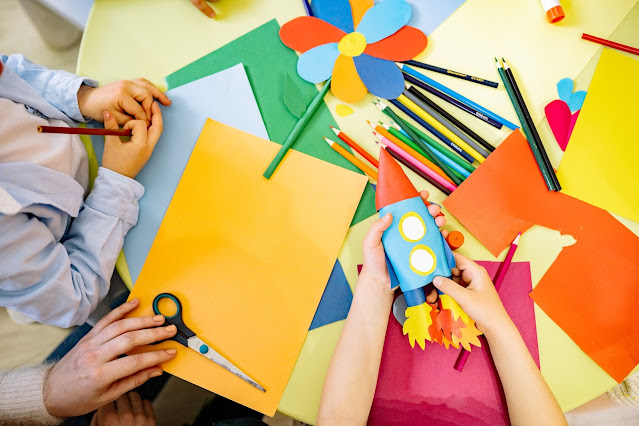 Two children and their grown-up crafting with colourful paper, pencils and scissors