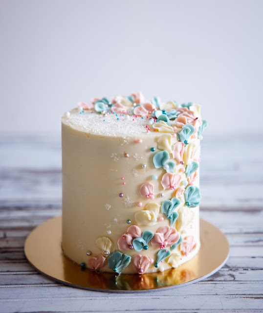 tall gender reveal cake with white frosting and blue and pink flowers