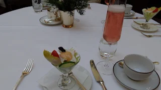 Table covered in white linens with a white porcelain tea cup on the right and a martini shaped glass filled with food in the center