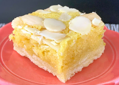 A Lemon Ginger Bakewell Bar with a pastry base topped with ginger curd and almond frangipane. Photographed on an orange plate