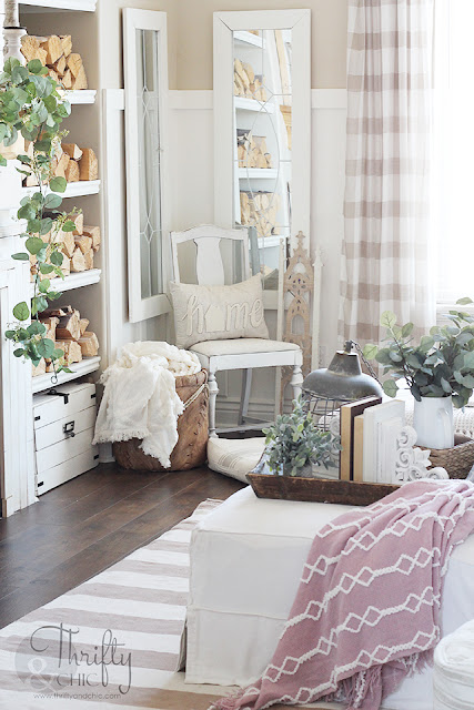 living room with white couch, large window, stacked wood, and shiplap mantel