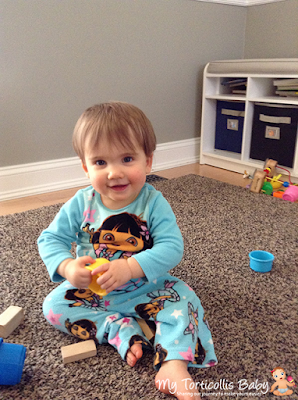 Happy baby with slight right torticollis playing with cup