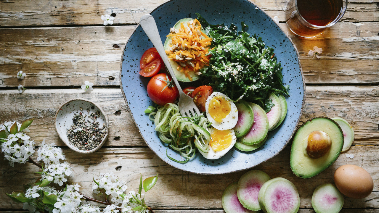 a bowl of food with eggs, avocado, and other vegetables on a wooden table -image 1