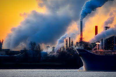 Ship sailing past chimneys of polluting smoke.