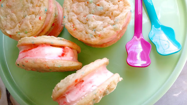 Birthday Cake Ice Cream Sandwiches sitting on a cake plate next to two spoons