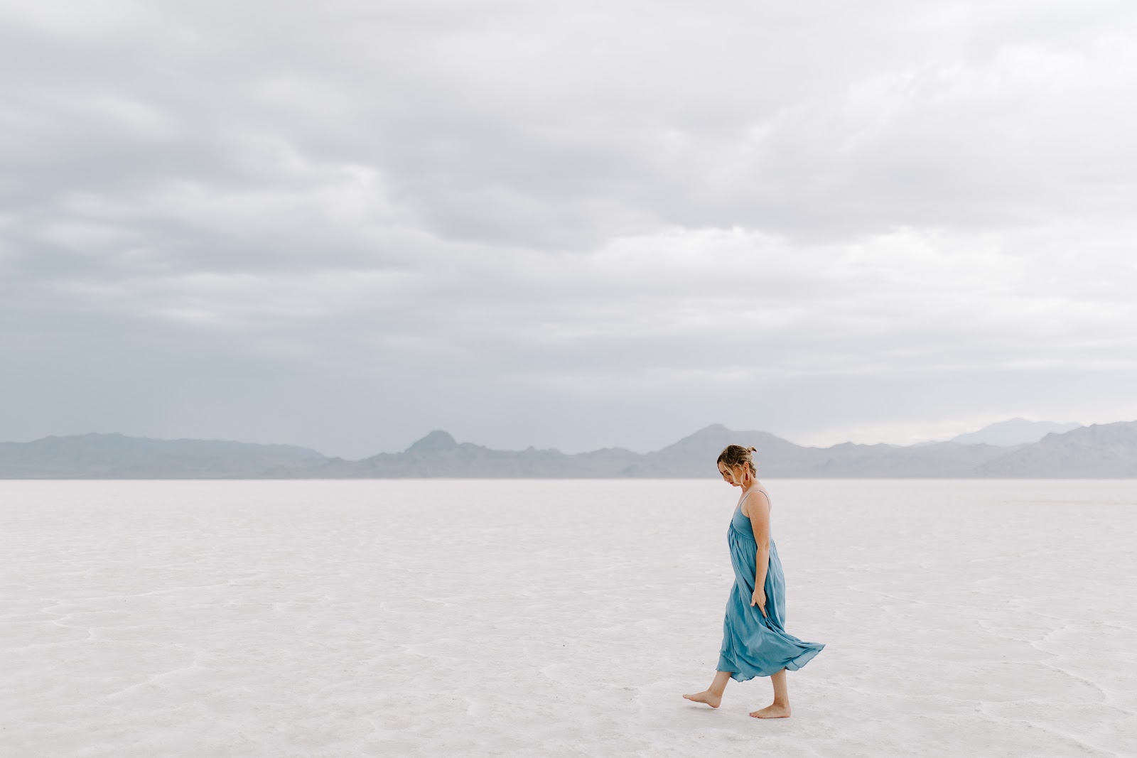 青いドレスを着た女性が白い砂の上を歩いている