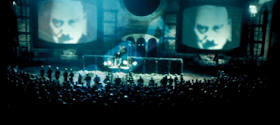 Big Brother's face looms on giant telescreens in Victory Square in one of several scenes of Michael Radford's 1984 film adaptation of George Orwell's Nineteen Eighty-Four.