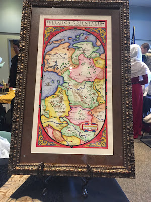 A large oval map in a decorative rectangular framing design, labeled "Belgica Orientalis" at the top, in an ornate old-gold frame.