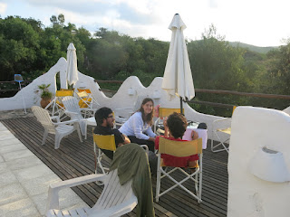 Three young people sitting and talking on an outdoor wooden deck.