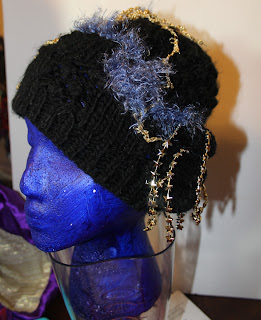 black hat with gold yarn and light blue eyelash yarn with strings of gold stars dangling below the edge on one side