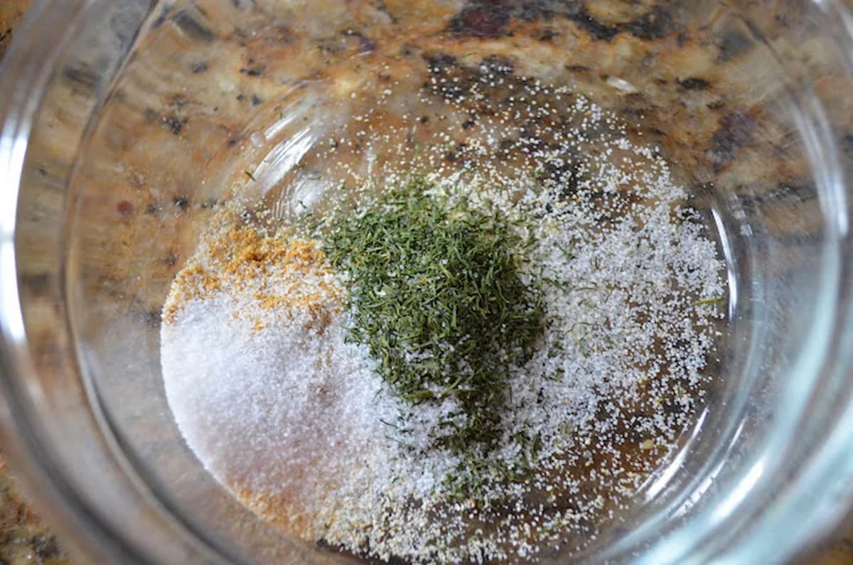 A down shot of a small glass bowl with granulated garlic, dried dill, cumin, and salt.
