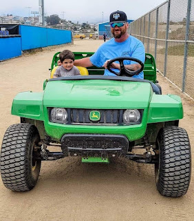 Josh doing field prep during a travelball tournament has a young helper with him