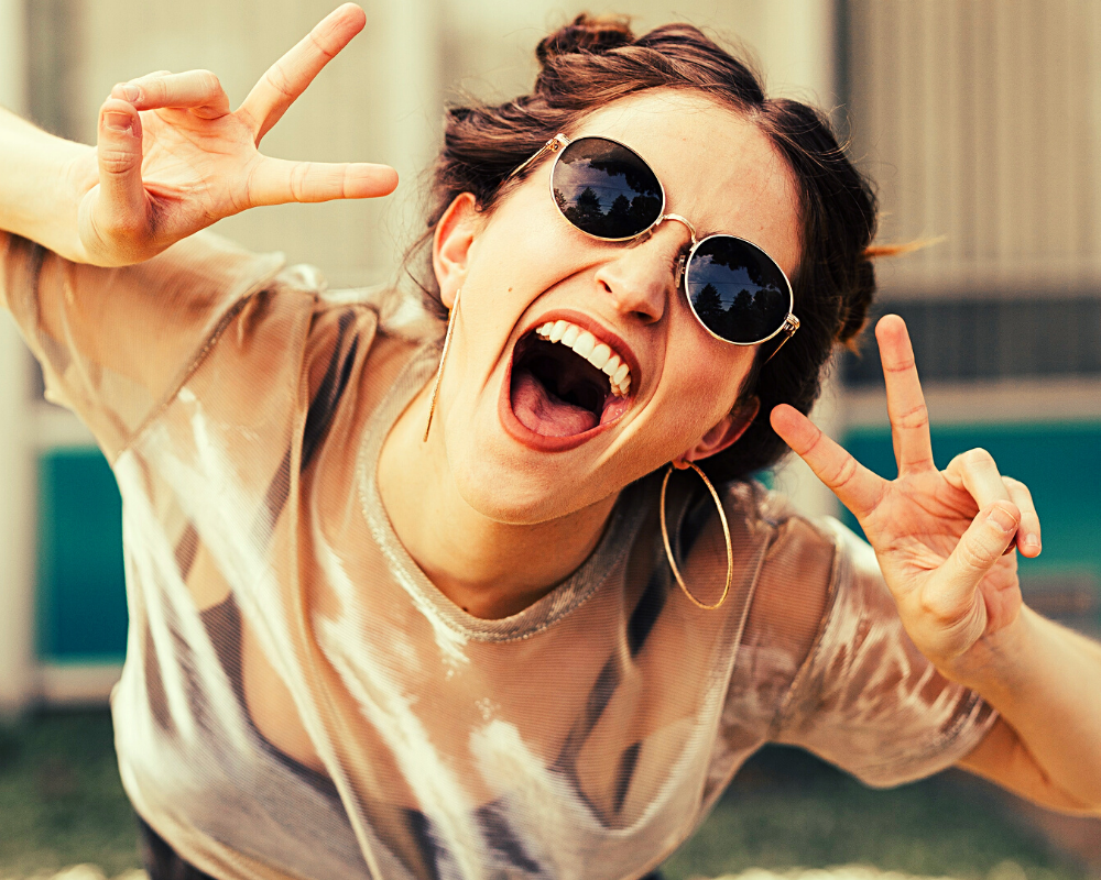 happy woman with bunches, sunglasses on, making peace signs on both hands